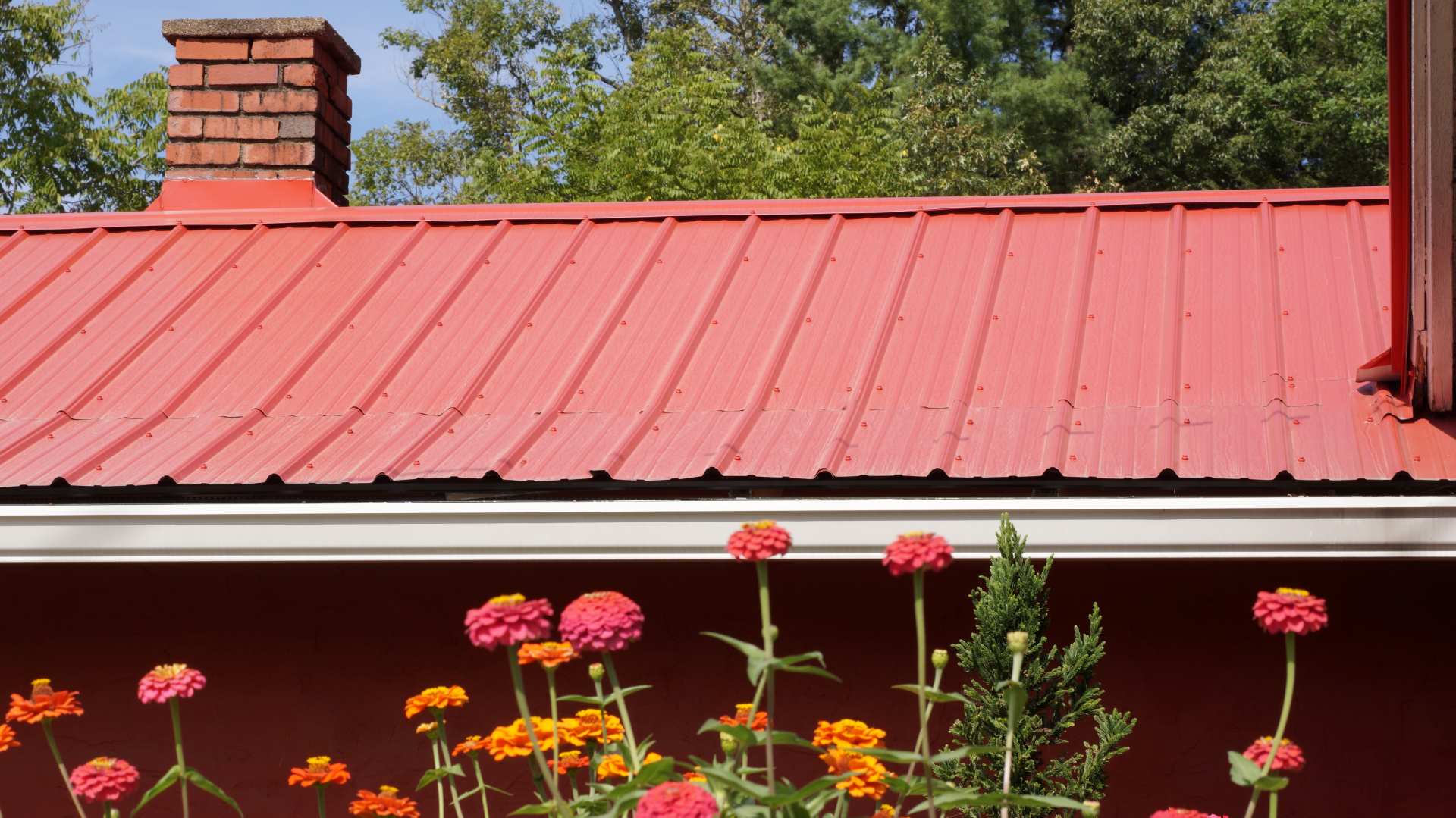 Red metal roof complemented by flowers | Featured image for the Metal Roof Repairs Landing Page from MHI Roofing. 